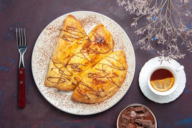 Vue de dessus de délicieuses pâtisseries cuites au four avec une tasse de thé sur l'espace sombre