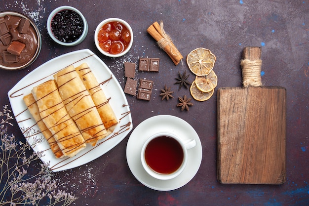 Vue de dessus de délicieuses pâtisseries sucrées avec de la confiture de chocolat et une tasse de thé sur un sol sombre cuire au four dessert sucre biscuit cake sweet