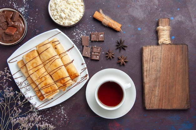 Vue de dessus de délicieuses pâtisseries sucrées avec du chocolat et une tasse de thé sur un bureau noir