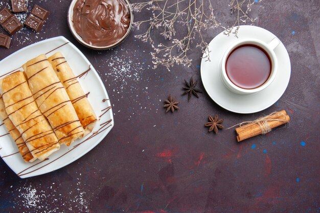 Vue de dessus de délicieuses pâtisseries sucrées avec du chocolat et une tasse de thé sur l'espace sombre