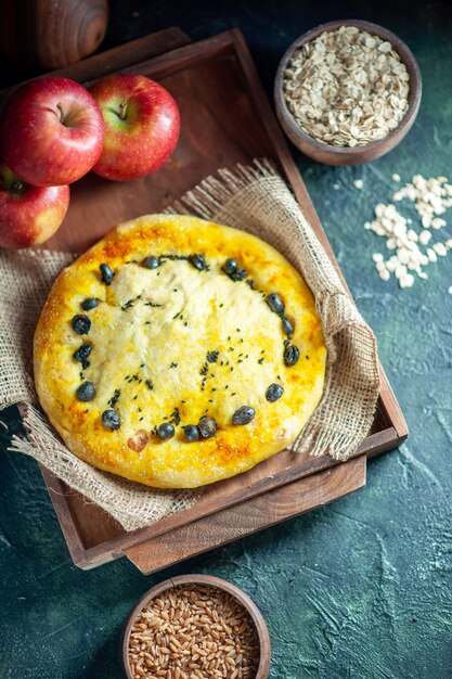 Vue de dessus de délicieuses pommes à pain sur planche de bois rectangle avoine et grains de blé dans des bols sur fond sombre