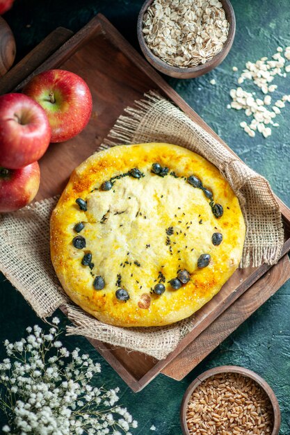 Vue de dessus de délicieuses pommes à pain sur planche de bois rectangle avoine et grains de blé dans des bols petites fleurs blanches sur table