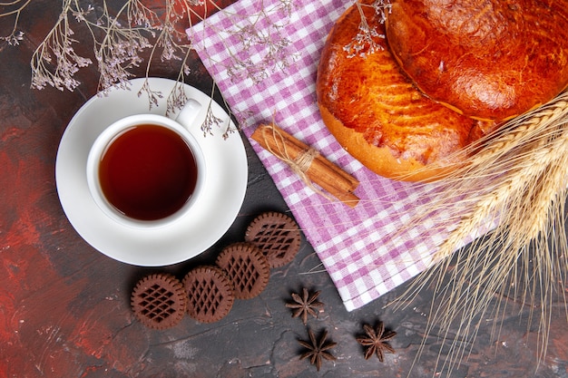 Vue de dessus de délicieuses tartes sucrées avec une tasse de thé sur le gâteau de table sombre pâtisserie tarte sucrée