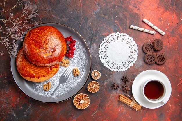 Vue de dessus de délicieuses tartes avec une tasse de thé sur la table sombre pâtisserie gâteau tarte sucrée