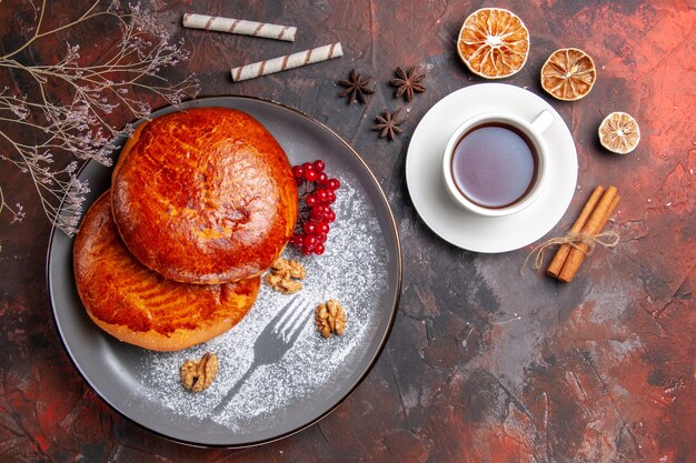 Vue de dessus de délicieuses tartes avec une tasse de thé sur la tarte à la pâtisserie gâteau sucré table sombre