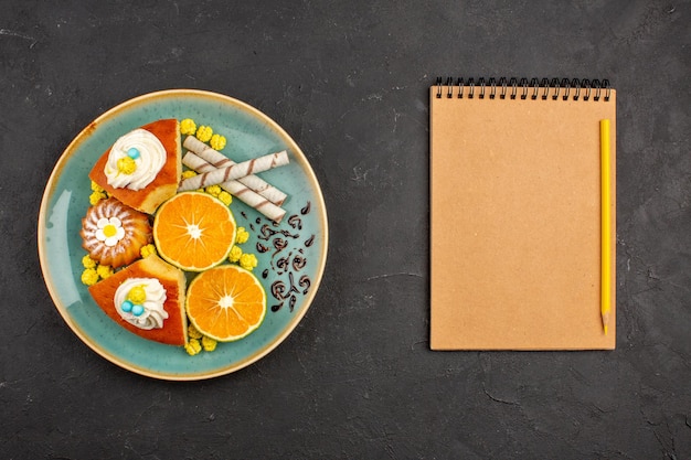 Vue de dessus de délicieuses tranches de gâteau avec des biscuits à la pipe et des mandarines tranchées sur fond gris foncé gâteau aux agrumes tarte biscuit thé sucré