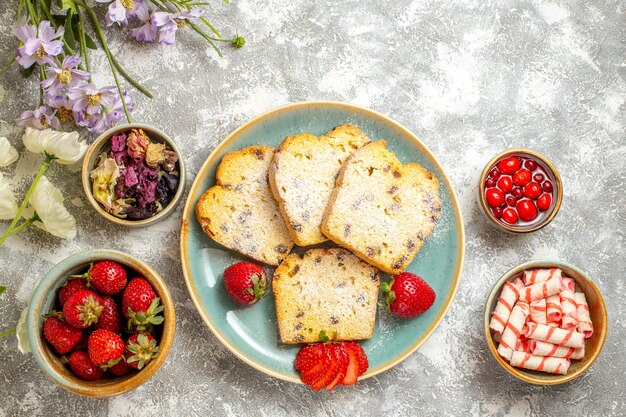 Vue de dessus de délicieuses tranches de gâteau avec des fraises et des bonbons à la lumière