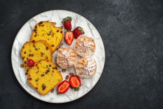 Vue de dessus de délicieuses tranches de gâteau avec des fraises rouges fraîches et des biscuits sur une surface gris foncé