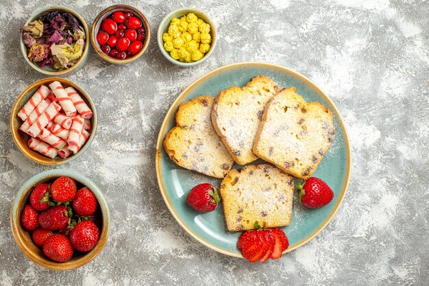 Vue de dessus de délicieuses tranches de gâteau avec des fruits et des bonbons sur des tartes sucrées de gâteau de surface légère