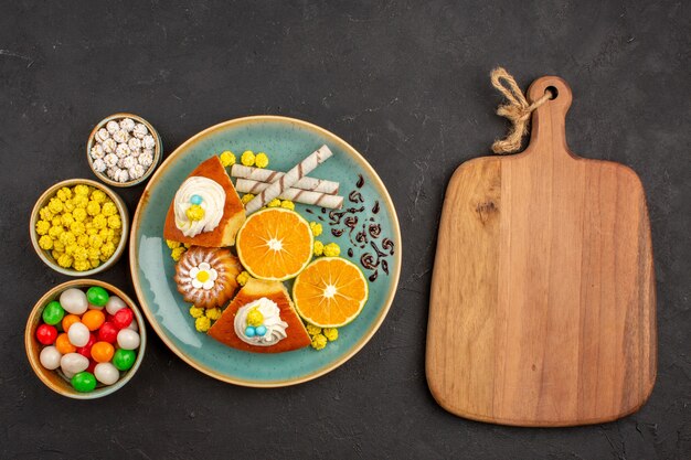 Vue de dessus de délicieuses tranches de gâteau avec des mandarines en tranches et des bonbons sur le noir