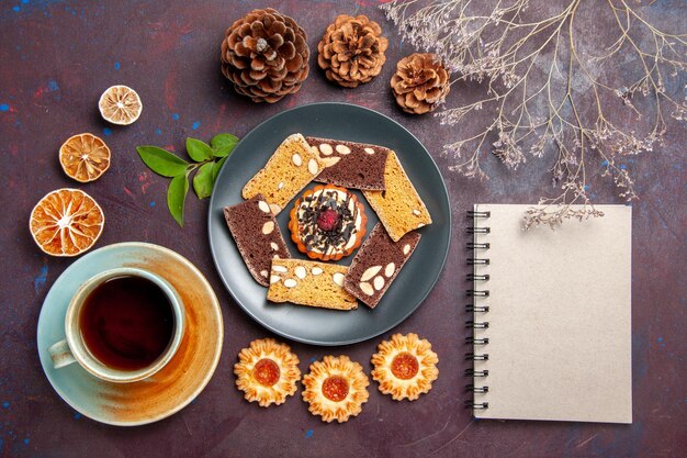 Vue de dessus de délicieuses tranches de gâteau avec petit biscuit et tasse de thé sur fond sombre biscuit biscuit dessert gâteau thé sucré