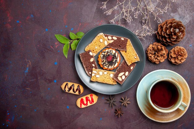 Vue de dessus de délicieuses tranches de gâteau avec une tasse de thé sur fond noir