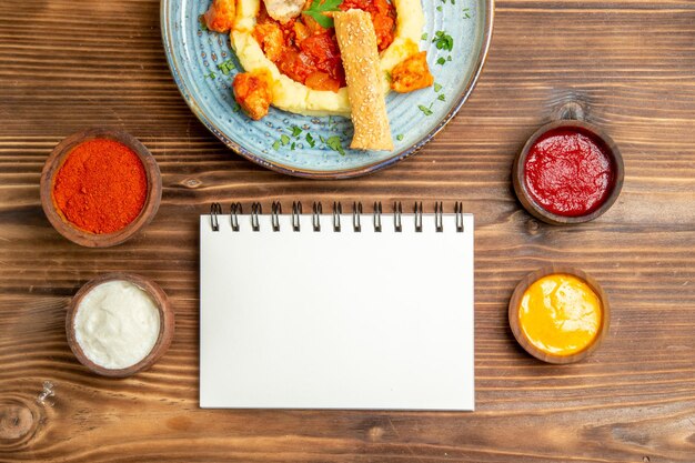 Vue de dessus de délicieuses tranches de poulet avec purée de pommes de terre et assaisonnements sur une table brune.