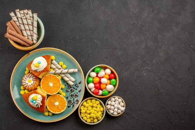 Vue de dessus de délicieuses tranches de tarte avec des mandarines fraîches et des bonbons sur le noir