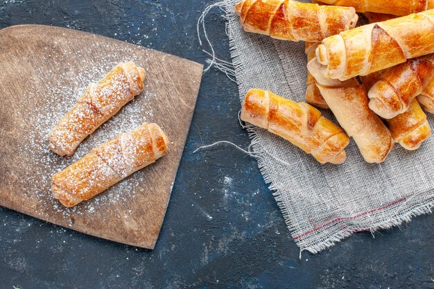 Vue de dessus de délicieux bagels sucrés en poudre et cuits au four sur un bureau gris foncé, faire cuire la pâte à pâtisserie biscuit sucre sucré