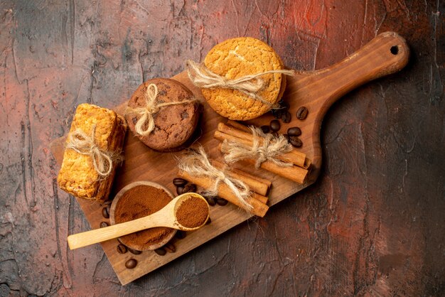 Vue de dessus de délicieux biscuits attachés avec une corde de cacao dans un bol de grains de café dans un bol de cannelle sur une planche de bois sur une table sombre