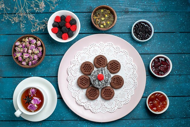 Vue de dessus de délicieux biscuits au chocolat avec de la confiture et une tasse de thé sur le gâteau de bureau rustique bleu thé au cacao biscuit sucré