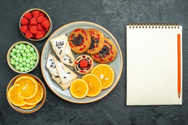 Vue de dessus de délicieux biscuits au sucre avec bloc-notes de pâtisseries et tranches d'orange sur une surface sombre biscuit au sucre gâteau sucré biscuit thé