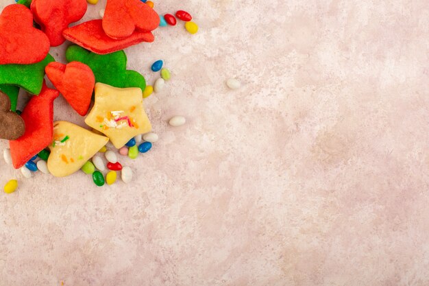 Vue de dessus de délicieux biscuits colorés différents formés avec des bonbons sur la surface rose