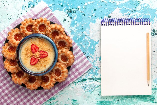 Vue de dessus de délicieux biscuits avec dessert aux fraises et bloc-notes sur une surface bleue