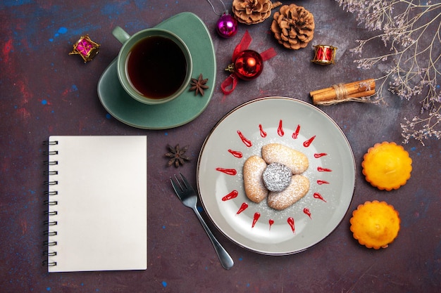 Vue de dessus de délicieux biscuits avec du sucre en poudre et une tasse de thé sur fond noir