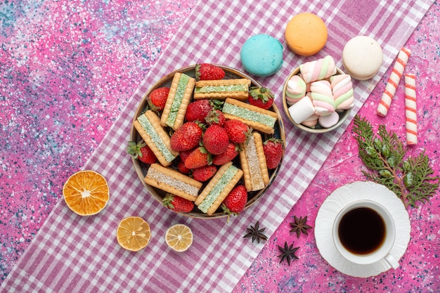 Vue de dessus de délicieux biscuits gaufres avec des fraises rouges fraîches et du thé sur une surface rose