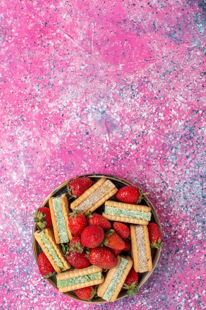Vue de dessus de délicieux biscuits gaufres avec des fraises rouges fraîches sur la surface rose