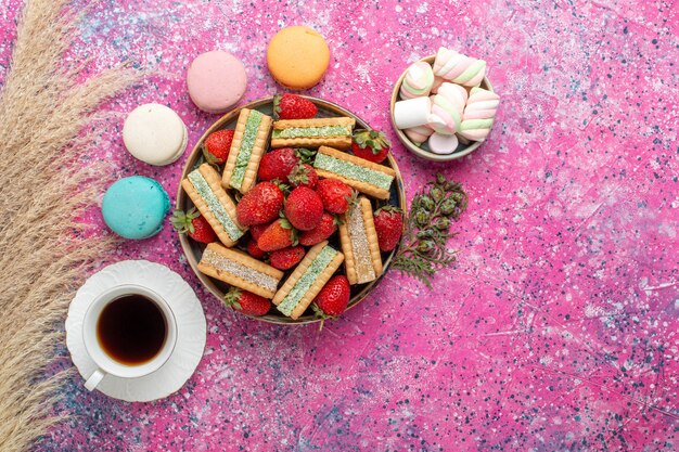 Vue de dessus de délicieux biscuits gaufres avec des macarons de fraises rouges fraîches et du thé sur une surface rose