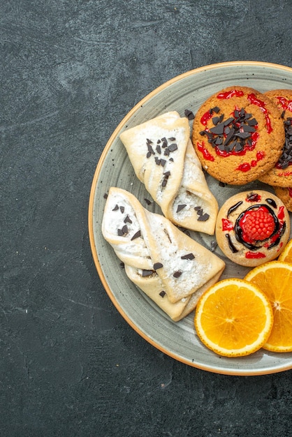 Vue de dessus de délicieux biscuits avec des pâtisseries fruitées et des tranches d'orange sur un bureau sombre tarte aux fruits gâteau sucré thé sucre