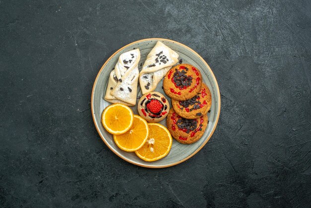 Vue de dessus de délicieux biscuits avec des pâtisseries fruitées et des tranches d'orange sur fond sombre tarte aux fruits gâteau sucré thé sucre