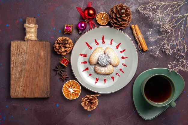 Vue de dessus de délicieux biscuits en poudre de sucre avec une tasse de thé sur fond noir