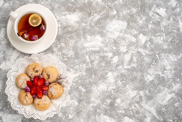 Vue de dessus de délicieux biscuits de sable aux fraises et tasse de thé sur une surface blanche