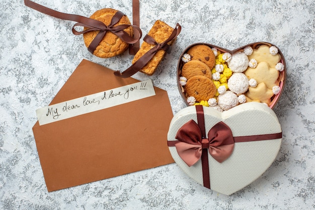 Vue de dessus de délicieux bonbons biscuits biscuits et bonbons à l'intérieur d'une boîte en forme de coeur sur fond blanc thé au sucre gâteau délicieux et sucré