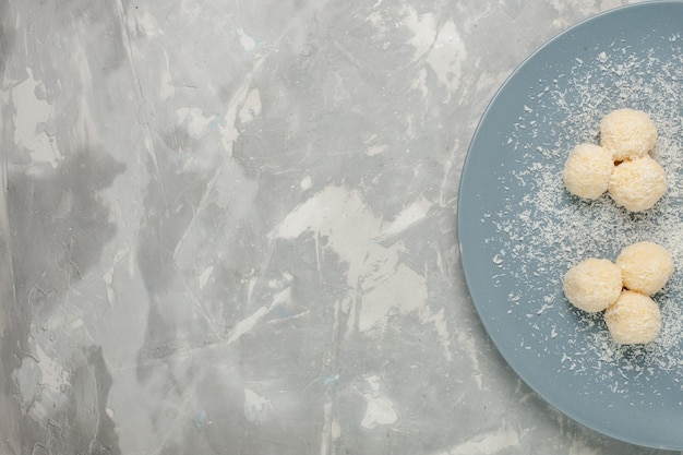 Vue de dessus de délicieux bonbons à la noix de coco à l'intérieur de la plaque bleue sur un bureau blanc