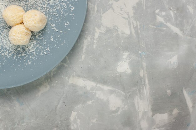 Vue de dessus de délicieux bonbons à la noix de coco à l'intérieur de la plaque bleue sur une surface blanche