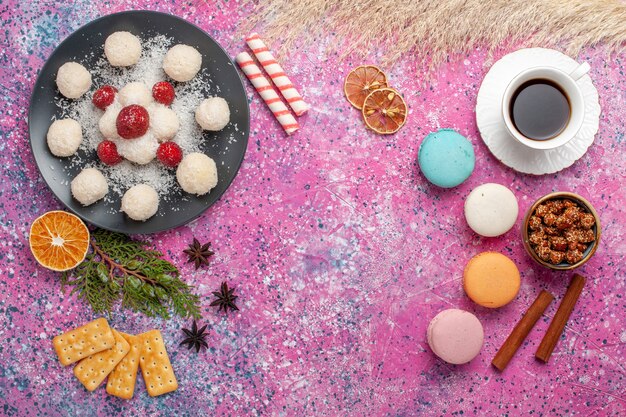 Vue de dessus de délicieux bonbons à la noix de coco avec des macarons français et une tasse de thé sur une surface rose clair