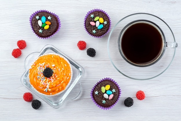 Une vue de dessus de délicieux brownies à l'intérieur des formes violettes avec une tasse de thé sur des bonbons de couleur blanc, bonbons