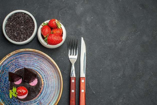 Vue de dessus délicieux cheesecake aux fraises et au chocolat sur des bols en assiette avec une fourchette et un couteau au chocolat aux fraises sur fond sombre isolé