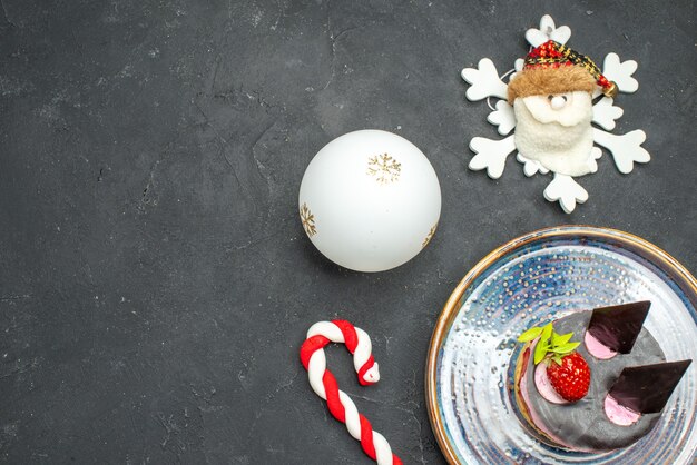 Vue de dessus délicieux cheesecake à la fraise et au chocolat sur des jouets de Noël à assiette ovale sur fond sombre isolé