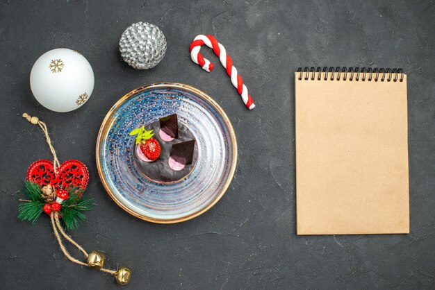 Vue de dessus délicieux cheesecake avec fraise et chocolat sur plaque ovale arbre de Noël jouets un cahier sur fond sombre isolé