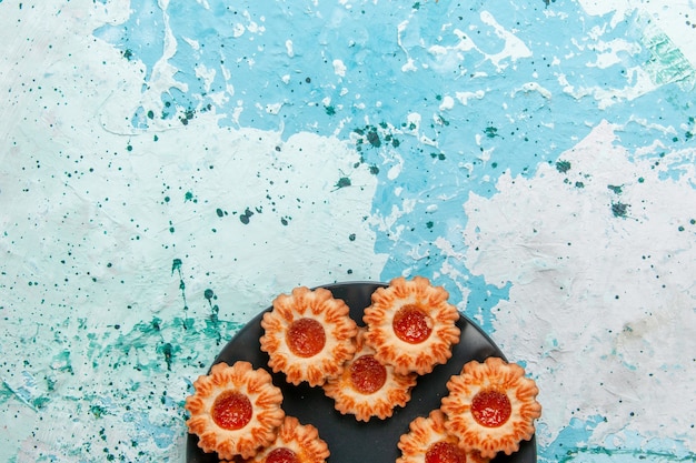 Photo gratuite vue de dessus de délicieux cookies avec de la confiture à l'intérieur de la plaque noire sur le bureau bleu clair biscuit biscuit thé sucré couleur sucre