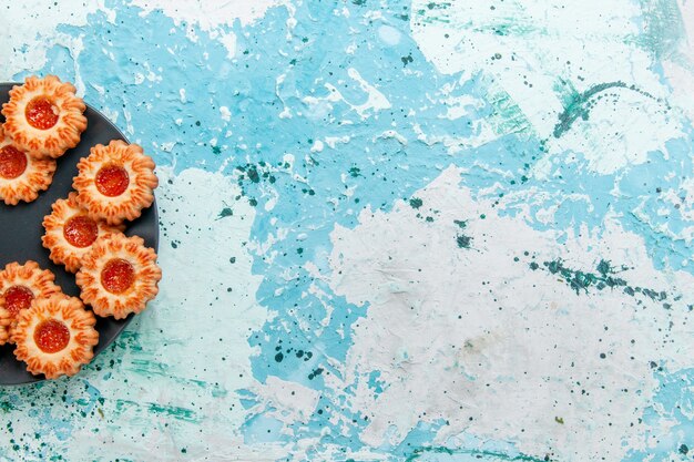 Vue de dessus de délicieux cookies avec de la confiture à l'intérieur de la plaque noire sur le bureau bleu clair biscuits biscuit thé sucré couleur