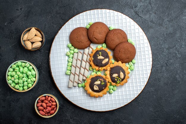 Vue de dessus de délicieux cookies avec différents bonbons sur fond gris foncé biscuit au sucre gâteau sucré tarte au thé cookies