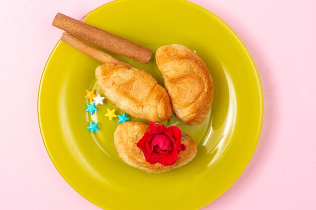 Vue de dessus de délicieux croissants cuits au four avec garniture de fruits à l'intérieur avec de la cannelle à l'intérieur de la plaque verte sur le fond rose