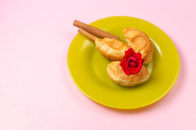 Vue de dessus de délicieux croissants cuits au four avec garniture de fruits à l'intérieur avec de la cannelle à l'intérieur de la plaque verte sur le fond rose