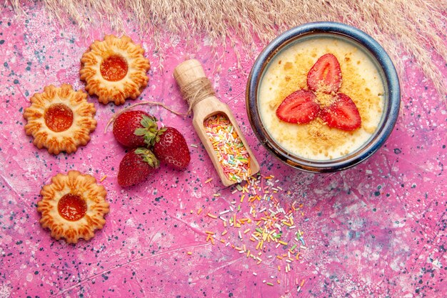 Vue de dessus délicieux dessert crémeux avec des fraises tranchées rouges et petits biscuits sur le sol rose clair dessert crème glacée aux baies crème aux fruits sucrés