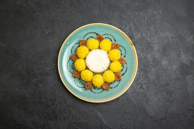 Vue de dessus délicieux dessert petits bonbons jaunes avec gâteau à l'intérieur de la plaque sur le fond gris bonbons thé sucre gâteau sucré