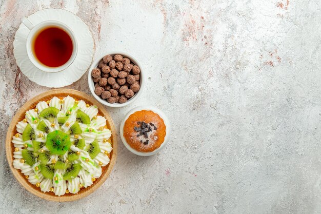 Vue de dessus délicieux dessert avec des tranches de kiwis et une tasse de thé sur fond blanc biscuit crème dessert aux fruits gâteau aux bonbons