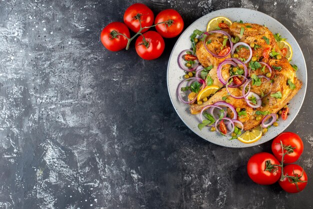 Vue de dessus d'un délicieux dîner plat de poulet frit avec diverses épices et aliments tomates avec tiges sur le côté gauche sur fond de couleur sombre