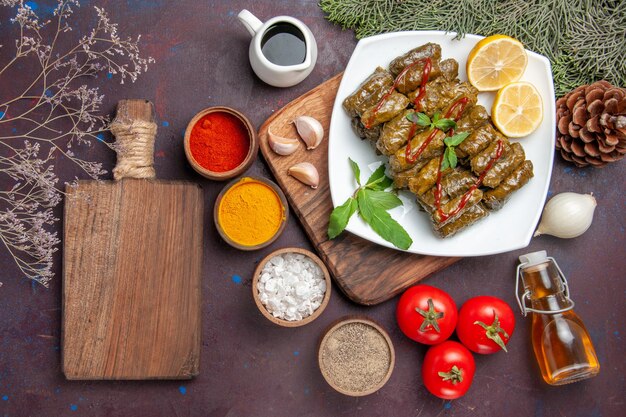 Vue de dessus de délicieux dolma de feuilles avec des tranches de citron et des assaisonnements sur le fond sombre plat de repas feuille de viande dîner nourriture